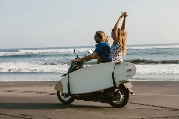 Vue latérale du couple équitation scooter avec planche de surf sur la plage à Bali, indonésie — Photo de stock