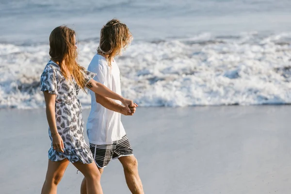 Vue latérale du couple se tenant la main et marchant sur la plage à bali, indonésie — Photo de stock