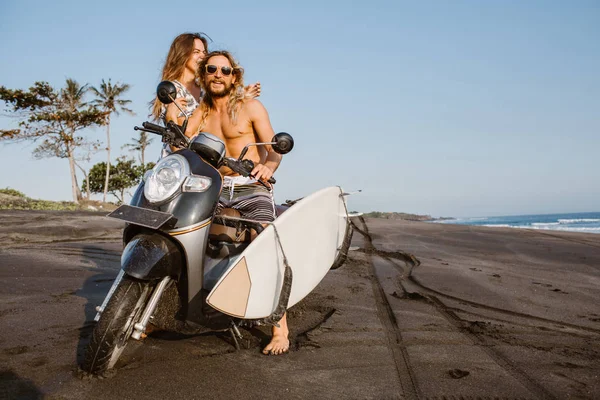Laughing couple with motorbike and surfing board on ocean beach in bali, indonesia — Stock Photo