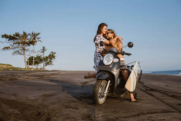 Novia sonriente abrazando novio en scooter en la playa en bali, indonesia - foto de stock