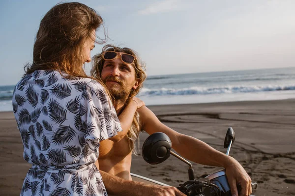 Novia abrazando novio en scooter en la playa y se miran el uno al otro en bali, indonesia - foto de stock