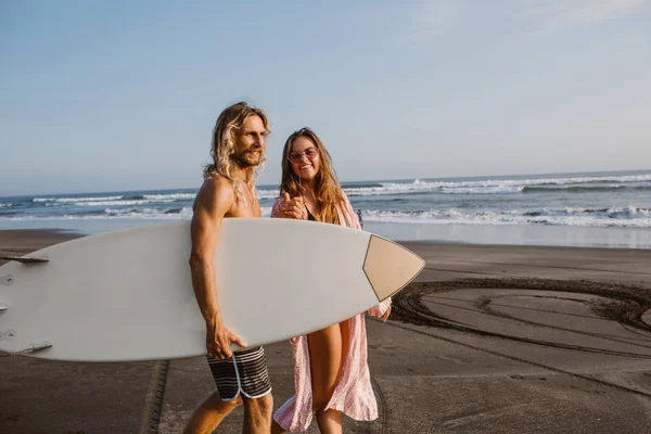 Happy couple walking together on beach with surfing board in bali, indonesia — Stock Photo