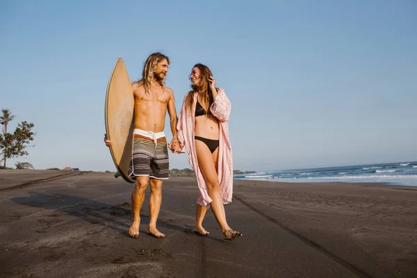 Couple walking on beach with surfing board and looking at each other in bali, indonesia — Stock Photo