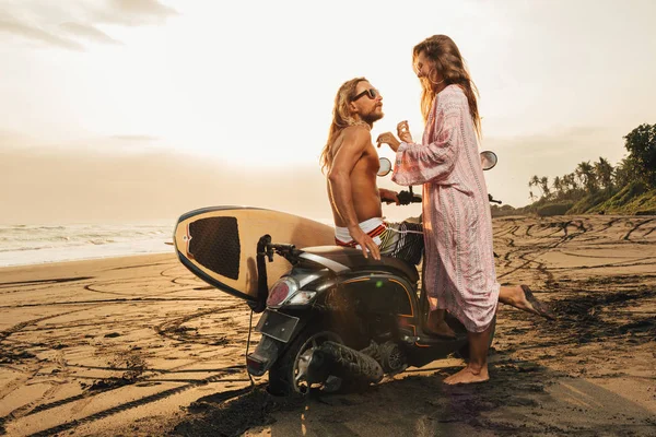 Side view of couple standing near scooter on beach during sunset in bali, indonesia — Stock Photo