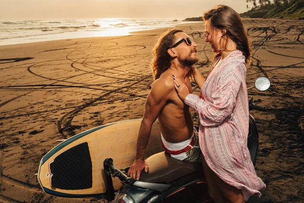 Smiling couple standing near scooter on beach and looking at each other in bali, indonesia — Stock Photo