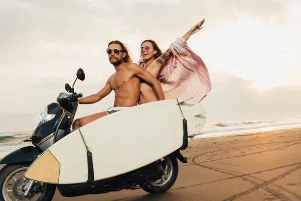 Pareja montando moto con tabla de surf en la playa en bali, indonesia - foto de stock