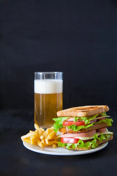 Sándwich en un plato y un vaso de cerveza sobre un fondo negro — Foto de Stock