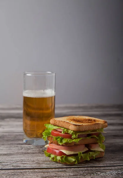 Sanduíche e um copo de cerveja em uma mesa de madeira — Fotografia de Stock