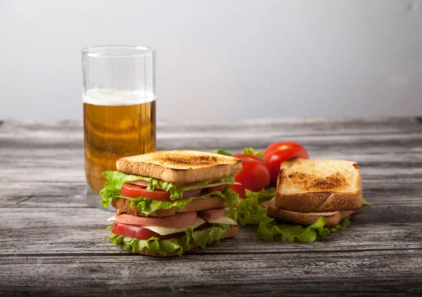 Sándwich, tomate, tostadas, ensalada y vaso con cerveza en un woo — Foto de Stock