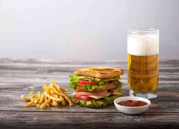 Sándwich con cerveza, papas fritas y salsa en una mesa de madera — Foto de Stock