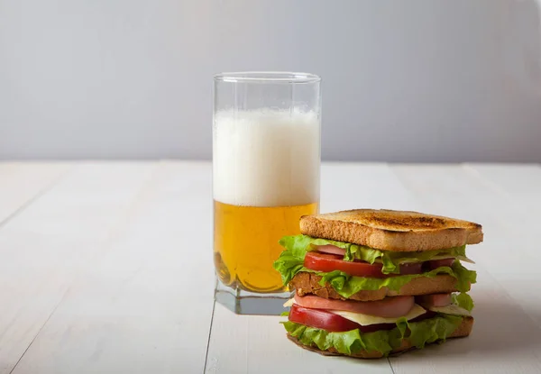 Sándwich y un vaso de cerveza sobre una mesa de madera blanca — Foto de Stock