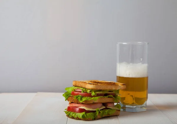 Sándwich y un vaso de cerveza en una mesa de madera — Foto de Stock