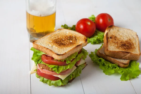 Sanduíche, tomate, torrada, salada e vidro com cerveja em madeira branca — Fotografia de Stock
