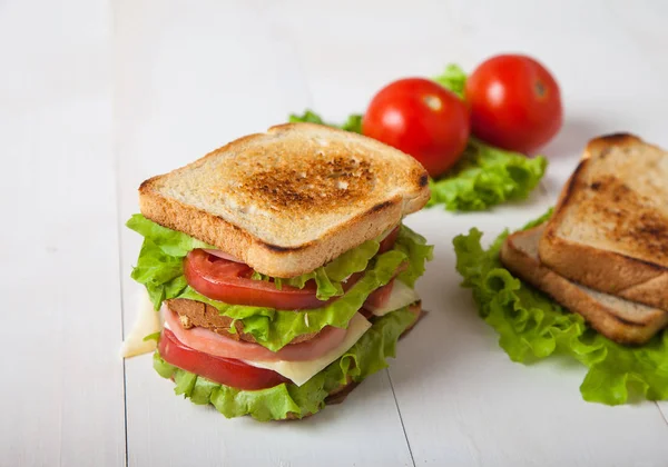 Sándwich, tomate, tostadas, ensalada sobre fondo de madera blanca — Foto de Stock