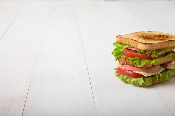 Sanduíche com carne e queijo está em uma mesa de madeira branca — Fotografia de Stock