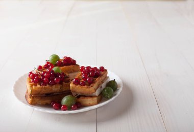 Beyaz ahşap bir masa üzerinde bir porselen tabakta kırmızı kuş üzümü ve Bektaşi ile Viyana waffle yalan
