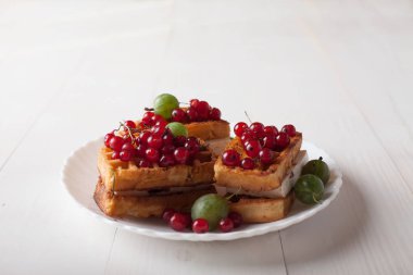 Beyaz ahşap bir masa üzerinde bir porselen tabakta kırmızı kuş üzümü ve Bektaşi ile Viyana waffle yalan