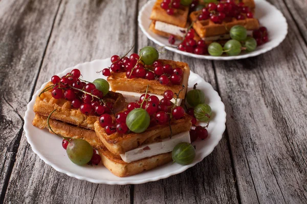 Ahşap bir masa üzerinde bir tabakta olgun çilek kırmızı kuş üzümü ve Bektaşi ile Viyana waffle yalan