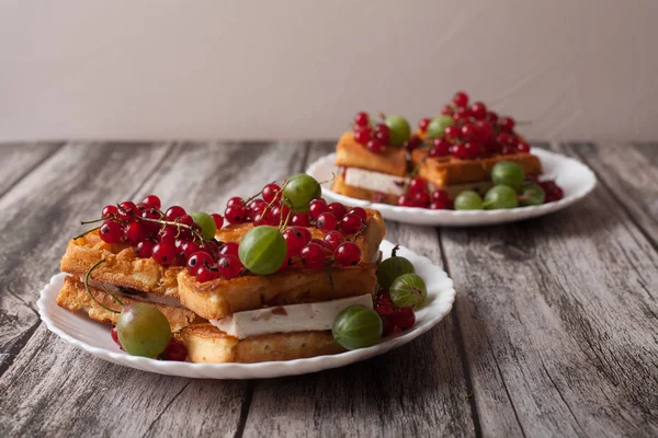 Ahşap bir masa üzerinde bir tabakta olgun çilek kırmızı kuş üzümü ve Bektaşi ile Viyana waffle yalan
