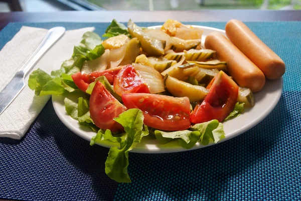 蒸し野菜と青のナプキンでテーブルの上の皿にサラダとソーセージ — ストック写真