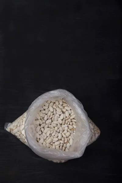 White beans in a plastic bag on a black background. concept. Tre — Stock Photo, Image