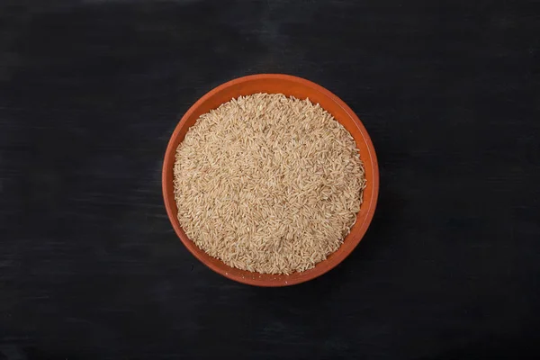 Unpolished rice in earthenware on black background. superfood — Stock Photo, Image