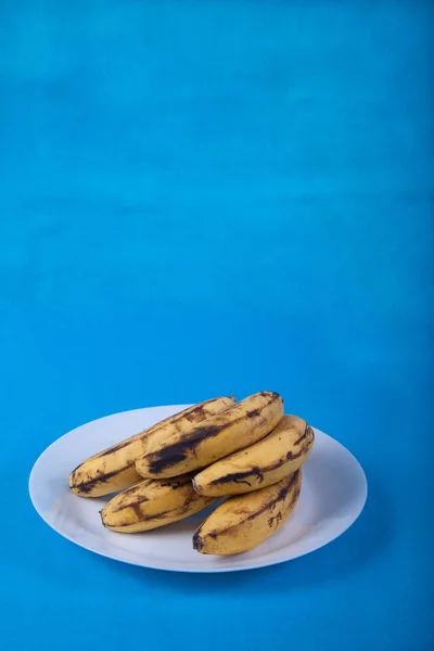 Уродливые бананы лежат на голубой фарфоровой тарелке на голубом фоне . — стоковое фото