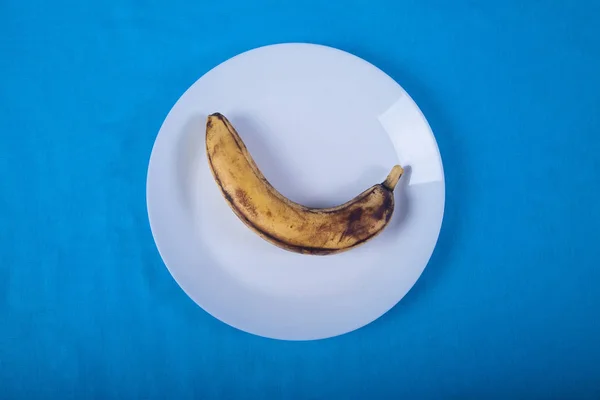 Уродливый банан лежат на голубой фарфоровой тарелке на голубом фоне . — стоковое фото