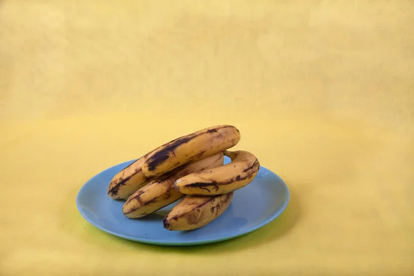 Hässliche Bananen liegen auf einem blauen Teller auf gelbem Grund. Kopie s — Stockfoto