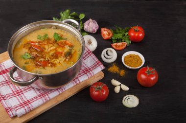 Kırmızı mercimek çorbası güveç siyah bir arka planda bir peçete üzerinde duruyor. Soğan, sarımsak ve baharatlar yakınında.