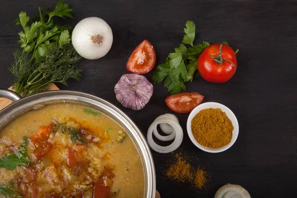 Rote Linsensuppe mit Tomaten, Zwiebeln, Knoblauch, Kräutern und Gewürzen in einer Metallpfanne auf schwarzem Hintergrund. — Stockfoto