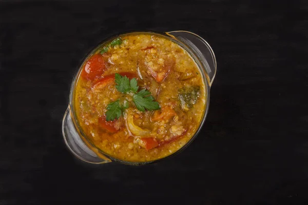 Red lentil soup in a glass bowl with spices, herbs, onion and garlic on a black background. Copy spaes. — Stock Photo, Image