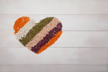 fasulye, mercimek ve fasulye bir kopyasını spaes ile beyaz ahşap bir arka plan üzerinde bir kalp şeklinde ortaya koydu, üst görünümü. Sağlıklı beslenme kavramı.