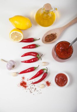 Cam bir kavanozda Harissa, kırmızı acı biber, limon, yağ, sarımsak ve beyaz bir arka plan üzerinde baharat ile bir kaşık. Dikey.