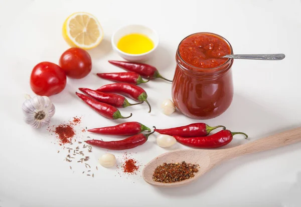 Harissa in een glazen pot, rode hete peper, citroen, olie, knoflook en een lepel met specerijen op een witte achtergrond. Horizontaal. — Stockfoto