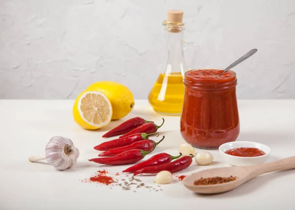 Harissa in een glazen pot, rode hete peper, citroen, olie, knoflook en een lepel met specerijen op een witte achtergrond. Selectieve focus — Stockfoto