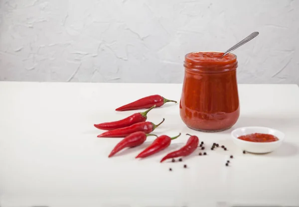 Harissa in einem Glas mit einem Löffel und Schoten roter Paprika auf weißem Hintergrund. horizontal — Stockfoto