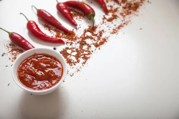 Harissa in een bord en rode chili peper, bestrooit met specerijen op een witte achtergrond. Selectieve focus. Kopiëren spaes — Stockfoto