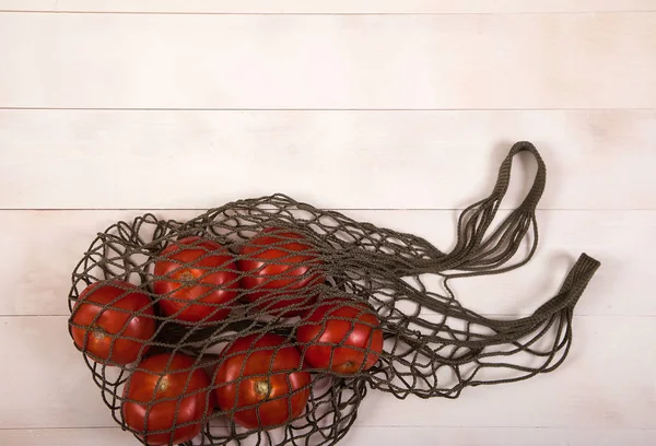 Los tomates rojos se encuentran en una bolsa elástica sobre un fondo de madera blanco — Foto de Stock