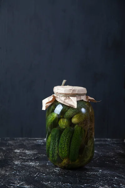 Pepinos fermentados en un frasco de vidrio sobre un fondo negro. Vertjical . — Foto de Stock
