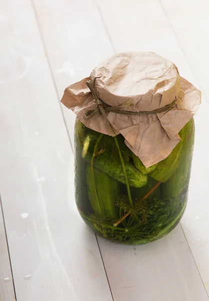 Fermented cucumbers in a glass jar on a white wooden background. Vertical — Stock Photo, Image