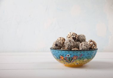 Susam tohumlu enerji topları beyaz ahşap bir masada seramik bir bardakta yatıyor. Vejetaryenlik. Kürekleri kopyala
