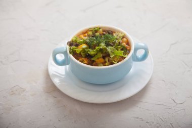 Açık beton arka planda mavi bir porselen bardakta sebze ve peynirli fasulye çorbası. Vejetaryen mutfağı