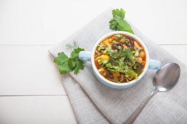 Fasulyeli sebze çorbası, peynir ve mavi porselen bir fincanda taze otlar açık beton arka planda keten bir peçetenin üzerinde duruyor. Sağlıklı yemek..