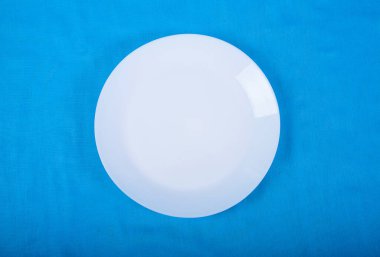 Boş beyaz porselen plaka mavi arka planda duruyor. Tabaklar.