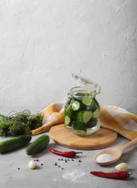 Küçük cam bir kavanozda mayalanmış salatalık, kapaklı, biberli, ahşap kaşık tezgahındaki tuz beton bir arka planda. Kürekleri kopyala.