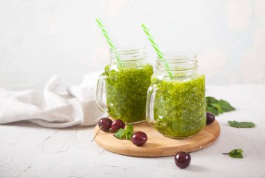 Cam kavanozlarda taze yeşil meyve suları ve beton bir arka planda ahşap bir stantta tatlı kirazlar. Kürekleri yatay kopyala