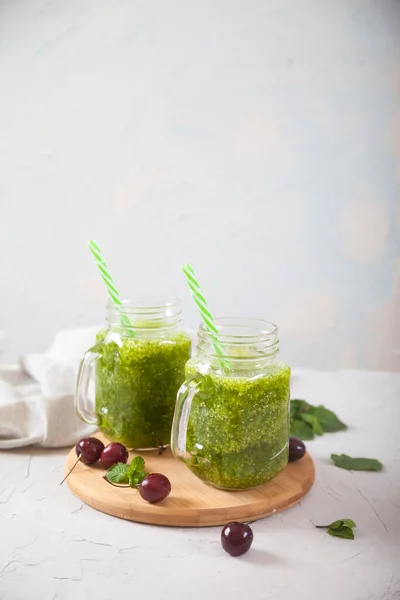 Cam kavanozlarda taze yeşil meyve suları ve beton bir arka planda ahşap bir stantta tatlı kirazlar. Kopyalama ögeleri