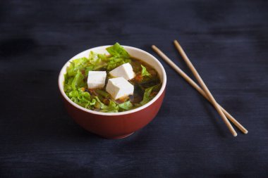 Tofu peyniri ve sebzeli Japon çorbası, siyah arka planda çubuklar.