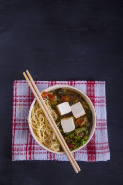 Sebze, makarna ve balıklı Japon çorbası, siyah arka planda kırmızı peçetedeki çubuklar.